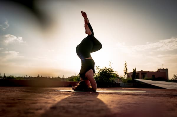 Silhouette en inversion (posture sur la tête Sirsasana) en plein air au coucher du soleil