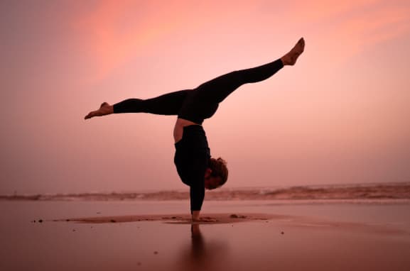 Pratiquante sur la plage en posture de handstand.