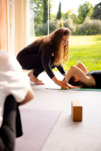 Manon Descroix, la fondatrice d'ĀYU YOGA SCHOOL aidant une élève à se préparer à la posture du pont