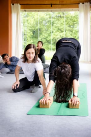 Formatrice ĀYU démontrant un exercice préparatoire avec une élève en formation de yoga