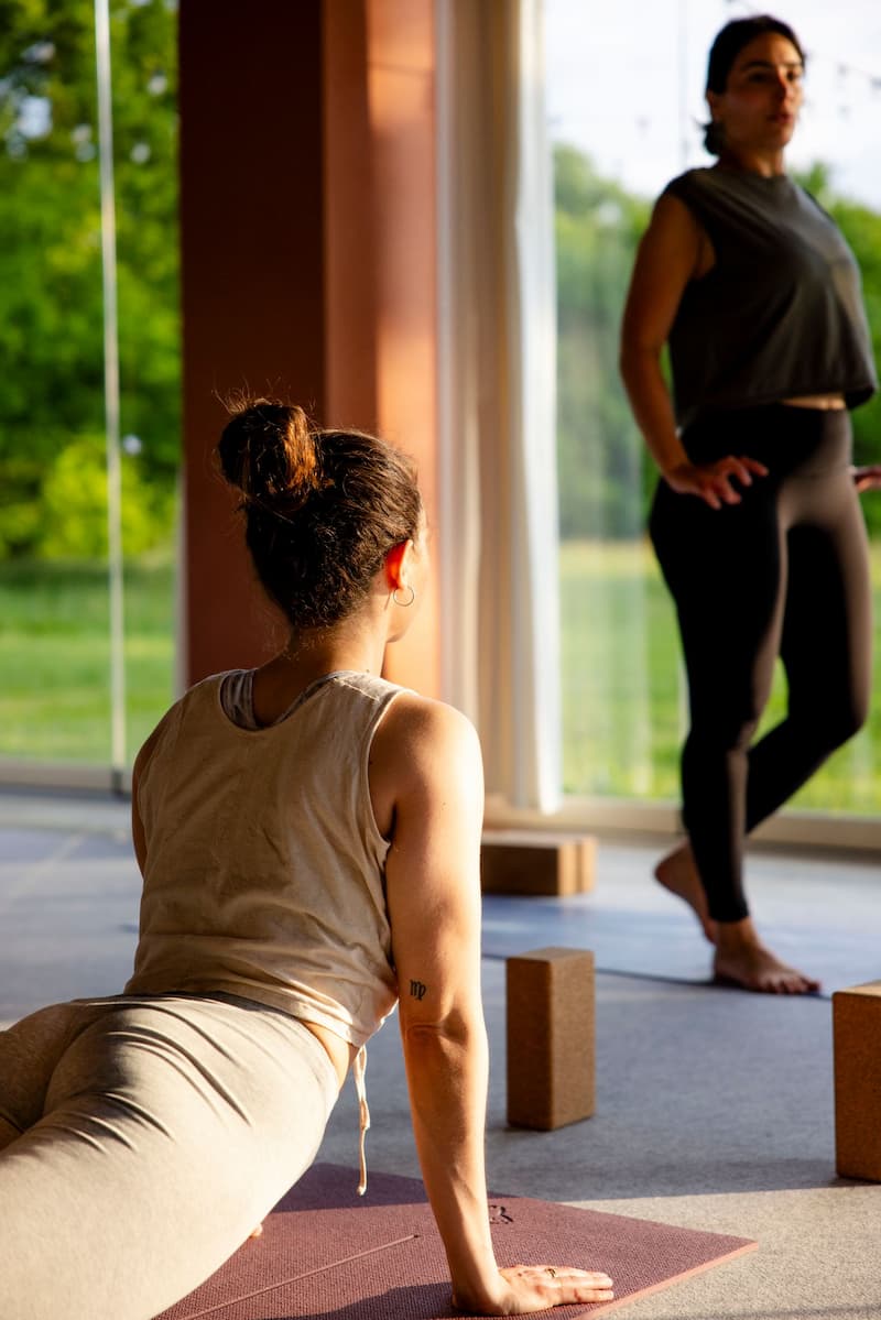 Une élève pratique le chien tête en haut sur son tapis pendant qu’une formatrice de yoga observe le groupe lors d’une formation 200h en présentiel